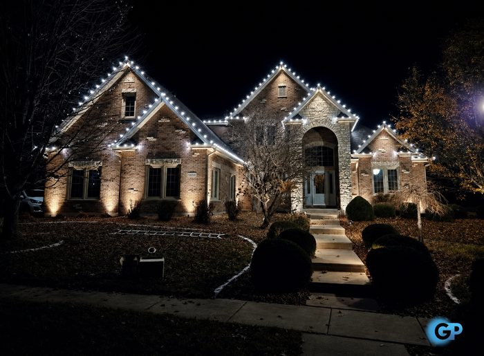 Warm white roofline and peak lighting with ground uplighting on a stone home