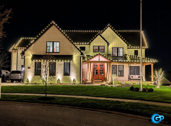 Warm white roofline lighting with lit garland and porch detail on a two-story home