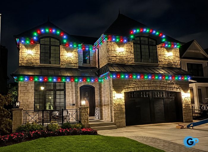 Multicolor C9 roofline lighting on a stone two-story home with a lit entry